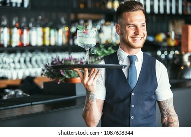 Smiling elegant waiter is holding a tray with a decorated cocktail ready to serve