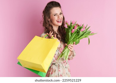 smiling elegant woman in floral dress with tulips bouquet and shopping bags isolated on pink background. - Powered by Shutterstock