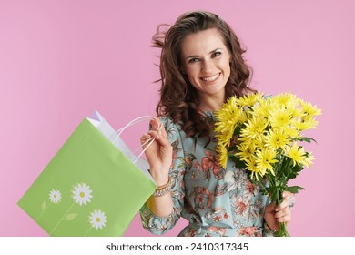 smiling elegant woman with long wavy brunette hair with yellow chrysanthemums flowers and green shopping bag isolated on pink background. - Powered by Shutterstock