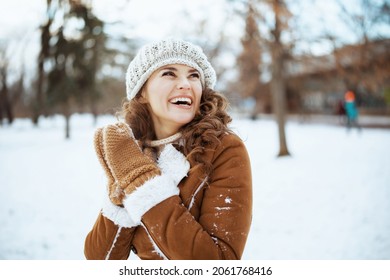 smiling elegant woman with mittens in a knitted hat and sheepskin coat outside in the city park in winter. - Powered by Shutterstock