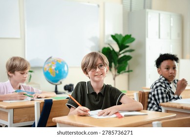 Smiling elementary school boy studying with notebook in bright classroom, happy childhood education and focused learning concept, Back to school