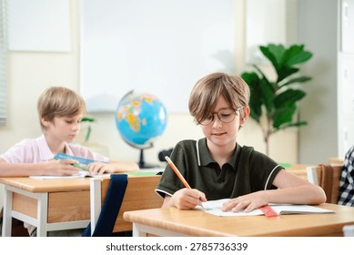 Smiling elementary school boy studying with notebook in bright classroom, happy childhood education and focused learning concept, Back to school