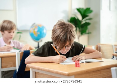 Smiling elementary school boy studying with notebook in bright classroom, happy childhood education and focused learning concept, Back to school