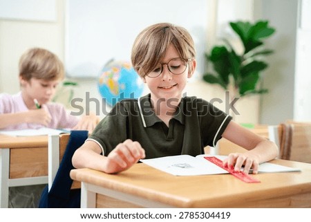 Smiling elementary school boy studying with notebook in bright classroom, happy childhood education and focused learning concept, Back to school