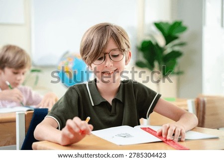 Smiling elementary school boy studying with notebook in bright classroom, happy childhood education and focused learning concept, Back to school