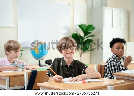 Smiling elementary school boy studying with notebook in bright classroom, happy childhood education and focused learning concept, Back to school