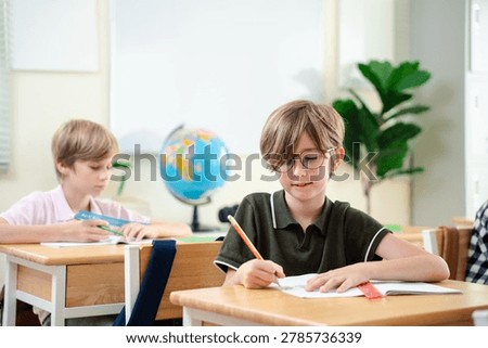 Smiling elementary school boy studying with notebook in bright classroom, happy childhood education and focused learning concept, Back to school