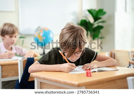 Smiling elementary school boy studying with notebook in bright classroom, happy childhood education and focused learning concept, Back to school