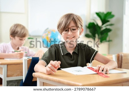 Smiling elementary school boy studying with notebook in bright classroom, happy childhood education and focused learning concept, Back to school