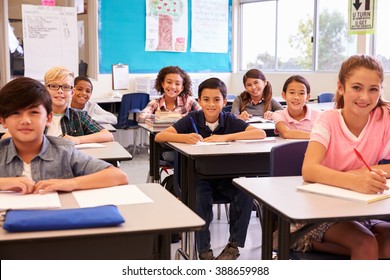 Smiling elementary school kids sitting at desks in classroom