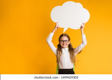 Smiling Elementary Student Girl Holding Speech Bubble Overhead On Yellow Studio Background. Thinking Of School. Mockup, Free Space