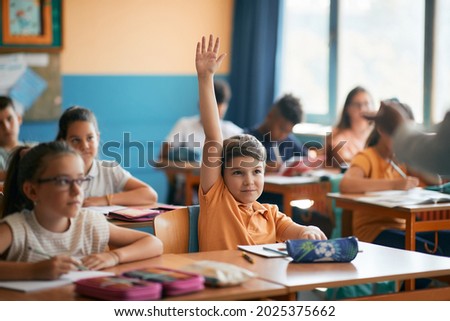 Smiling elementary student raising his hand to answer a question during class at school. 