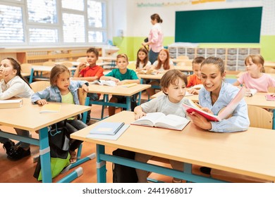 Smiling elementary teacher reading book to schoolgirl in classroom - Powered by Shutterstock