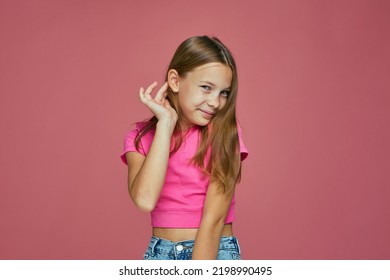 Smiling Embarrassed Shy Caucasian Child Girl Fixing Her Hair Posing On Pink Studio Background. Children's Fashion