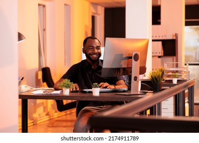 Smiling employee working on computer to do research on network, planning business project online. Analyzing paperwork data to write email report, web presentation during sunset in office. - Shutterstock ID 2174911789