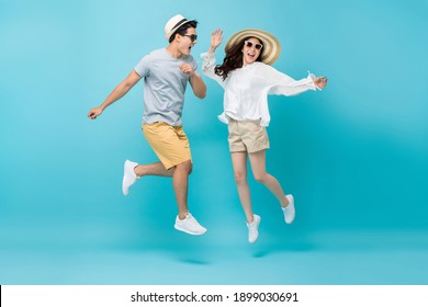 Smiling Energetic Asian Couple Tourists In Summer Beach Casual Clothes Jumping Isolated On Light Blue Studio Background