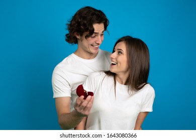 Smiling engaged couple with proposal ring isolated on blue background.