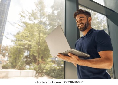 Smiling entrepreneur working on laptop standing in modern coworking near windows during working day - Powered by Shutterstock