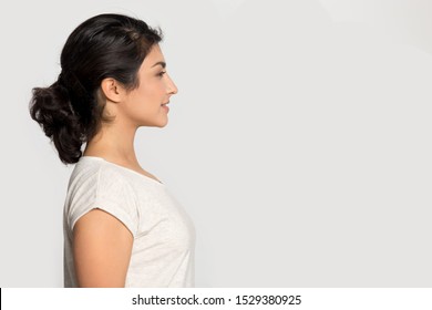 Smiling ethnic young woman stand in profile isolated on grey studio background look at blank copy space aside, happy millennial indian girl look to side consider good sale offer deal or discount