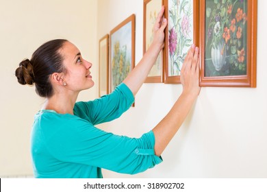 Smiling European Girl Hanging  Pictures In Frames On Wall At House