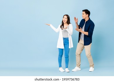 Smiling excited Asian couple tourists pointing hands to empty space aside on isolated light blue background