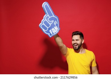 Smiling excited overjoyed young bearded man 20s in yellow t-shirt cheer up support favorite sport team look aside hold fan foam glove finger up isolated on plain dark red background studio portrait - Powered by Shutterstock