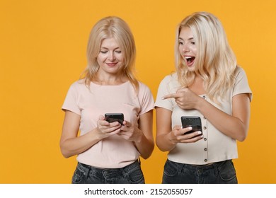 Smiling Excited Shocked Family Two Women Blonde Mother Daughter In Casual Clothes Pointing Index Finger On Mobile Phone Typing Sms Message Isolated On Bright Yellow Colour Background Studio Portrait