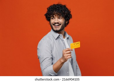 Smiling excited vivid exultant fascinating young bearded Indian man 20s years old wears blue shirt hold in hand show credit bank card looking aside isolated on plain orange background studio portrait - Powered by Shutterstock