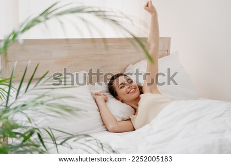 Smiling excited young woman in casual casual clothes lying in bed hands stretching eyes closed rest relax spend time in bedroom lounge home in own room house wake up dream be lost in reverie good day