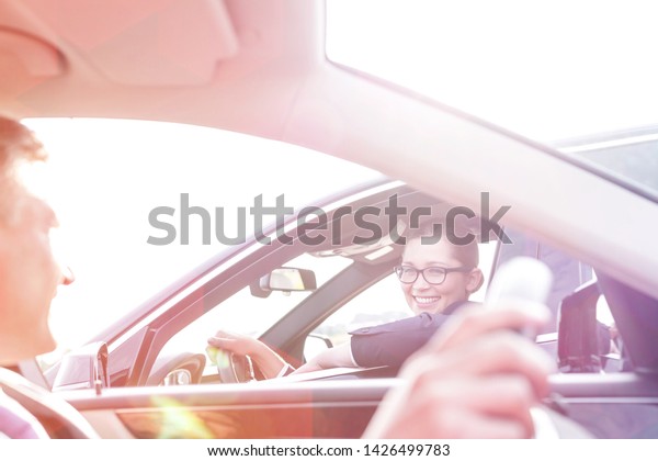Smiling executive and businesswoman talking while\
sitting in cars