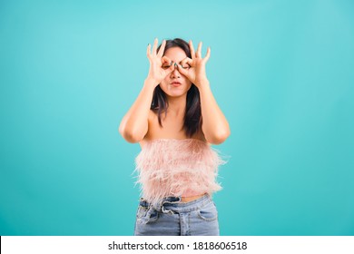 Smiling Face Asian Beautiful Woman Her Showing OK Hand Sign Over Her Both Eye And Pucker Up Lips On Blue Background, With Copy Space For Text