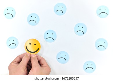 A smiling face icon among a group of sad emoticons in white background. Be positive and stay happy concept. - Shutterstock ID 1672285357