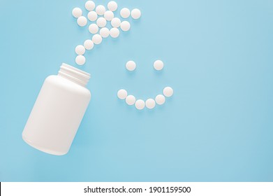 smiling face lined with pills. White jar and scattered white pills. Smiling face made from white round pills on blue background. Medicine and health care concept. Top view. copy space