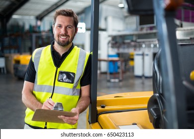 Smiling factory worker writing on clipboard in factory - Powered by Shutterstock