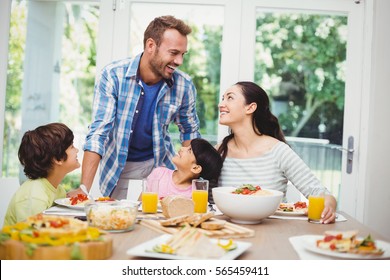 Smiling Family Discussing At Dining Table In Home