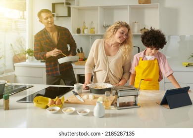 Smiling Family Following Tutorial On Tablet Computer When Making Pasta At Home