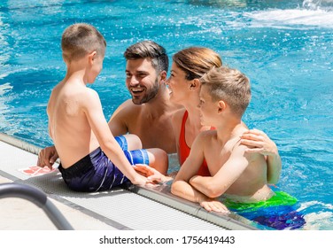 Smiling Family Of Four Having Fun And Relaxing In Indoor Swimming Pool At Hotel Resort.