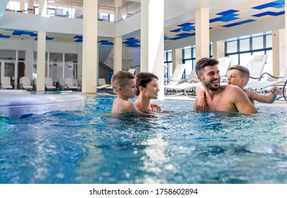 Smiling Family Of Four Having Fun And Relaxing In Indoor Swimming Pool At Hotel Resort.