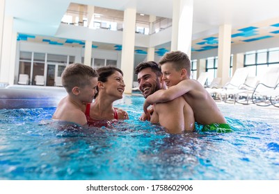 Smiling Family Of Four Having Fun And Relaxing In Indoor Swimming Pool At Hotel Resort.