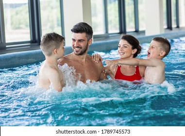 Smiling Family Of Four Having Fun And Relaxing In Indoor Swimming Pool At Hotel Resort.