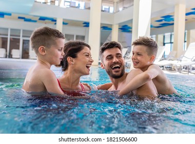 Smiling family of four having fun and relaxing in indoor swimming pool.