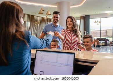 Smiling family of four in the hotel lobby check in at the reception for vacation. - Shutterstock ID 1853041003