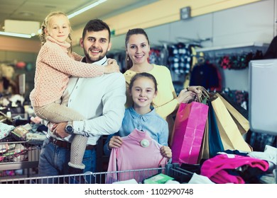 Smiling Family Of Four With Shopping Bags In Clothing Shop