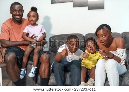 Smiling family of four with two kids sitting on sofa at home, radiating joy and togetherness and wathing tv