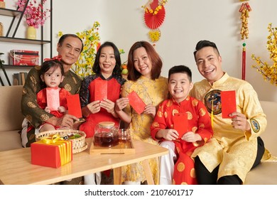 Smiling family members in ao dai dresses holding red lucky money envelopes