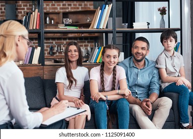 smiling family on therapy session by female counselor writing in clipboard in office 