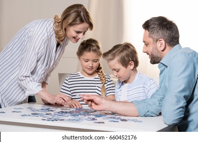 Smiling Family Playing With Puzzle On Table At Home Together