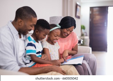 Smiling Family Reading Magazine While Sitting On Sofa At Home