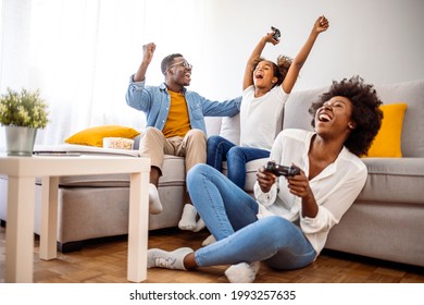 Smiling Family Sitting On The Couch Together Playing Video Games. Family Sitting On The Couch Together Playing Video Games, Selective Focus.Happy Family Sitting On A Sofa And Playing Video Games