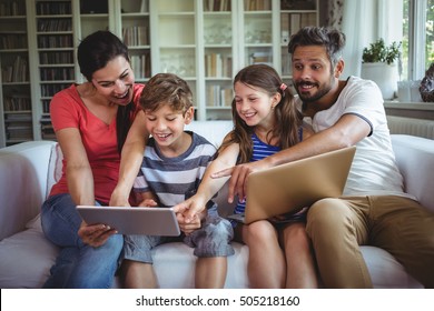 Smiling family sitting on sofa and pointing at digital tablet at home - Shutterstock ID 505218160